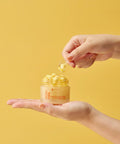 Hand holding a jar of skincare product with a yellow background