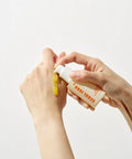 Person applying a yellow substance from a tube labeled 'SEOUL 1988' on a white background