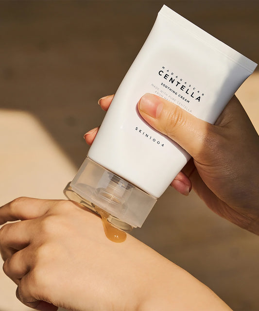 Close-up of hands dispensing the golden-amber gel texture of SKIN1004 Madagascar Centella Soothing Cream from the tube onto a hand