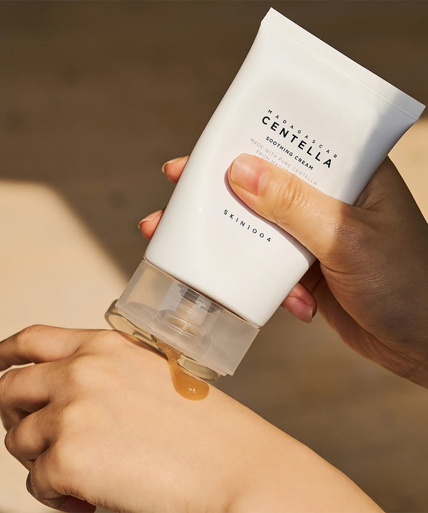 Close-up of hands dispensing the golden-amber gel texture of SKIN1004 Madagascar Centella Soothing Cream from the tube onto a hand