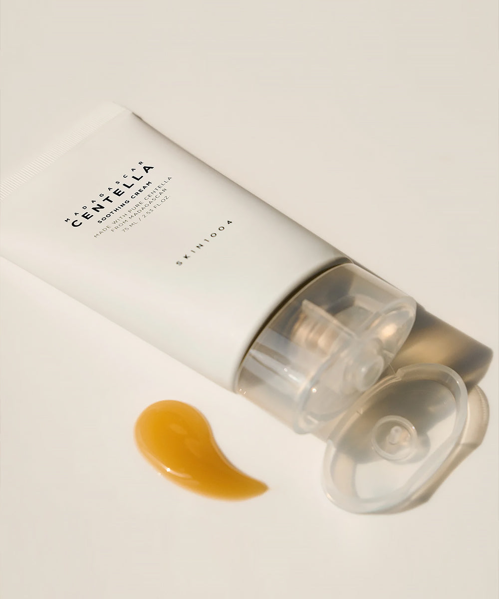 Top-down view of an open SKIN1004 Madagascar Centella Soothing Cream tube with the clear cap removed, lying next to a large dollop of its golden gel texture