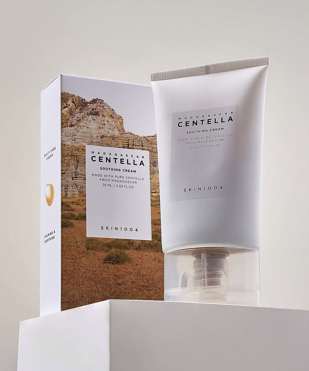 The SKIN1004 Madagascar Centella Soothing Cream tube standing on a white plinth next to its landscape-printed external product packaging box