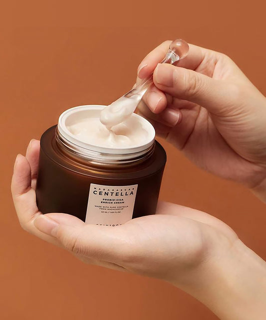 Person holding a jar of cream with a dropper over it against a brown background