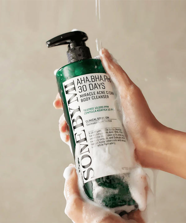 Hand holding a bottle of Some By Mi AHA BHA 30 Days Miracle Acne Clear Body Cleanser with a beige background.