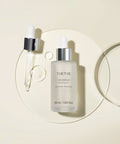 TIRTIR SOS Serum bottle and dropper on a circular glass tray, showcasing clear, hydrating serum droplets against a neutral beige background