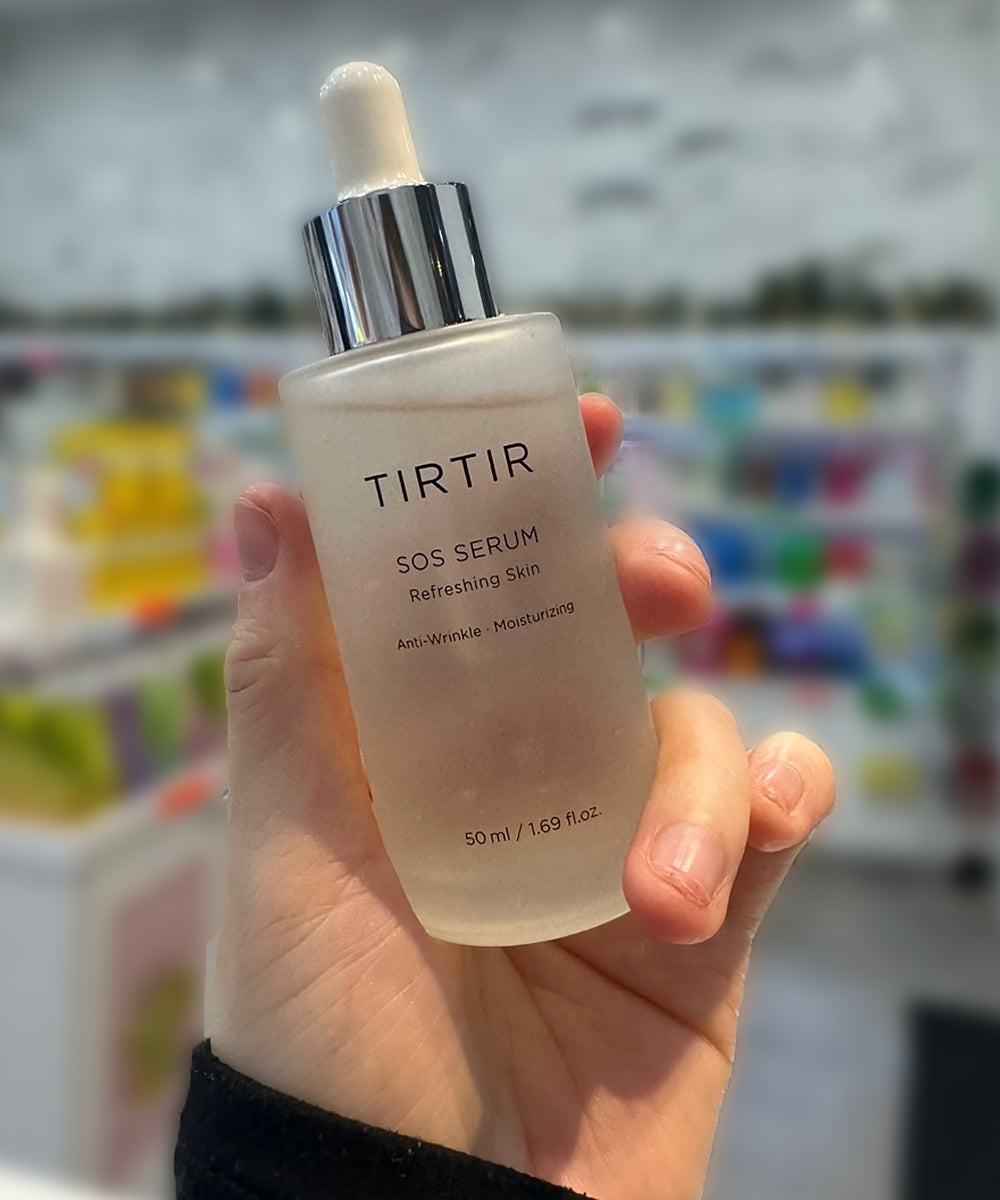 A person holding the TIRTIR SOS Serum bottle, demonstrating the product size and frosted glass packaging in a retail setting