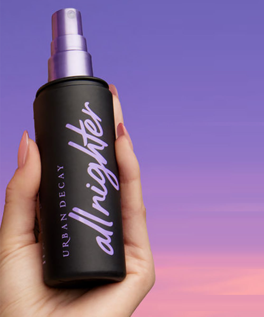 Hand holding a black spray bottle labeled 'allnighter' by Urban Decay against a gradient background.