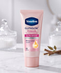Vaseline Glutaglow Ampoule Ultra Bright dry serum deodorant tube in pink, set on a marble surface with decorative glass jars and dried leaves in the background.