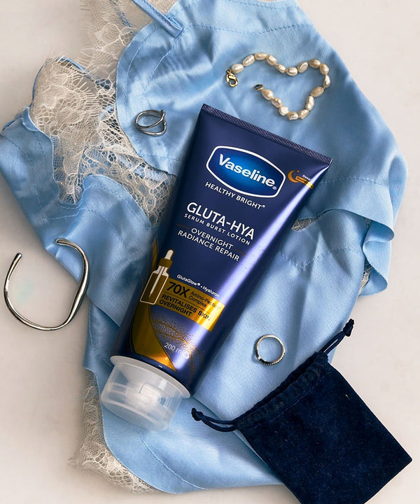 Vaseline Gluta-Liya tube on a blue fabric background with jewelry and a map.
