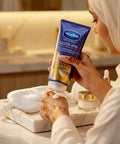 Person applying Vaseline Gluta-Hya serum to their hand in a bathroom setting
