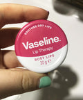 Vaseline lip therapy container held by a hand with green nail polish.