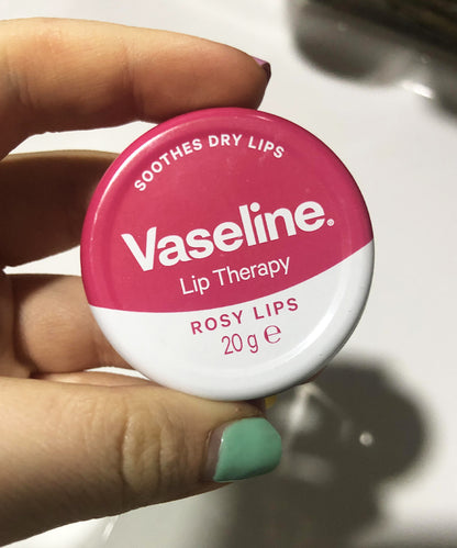 Vaseline lip therapy container held by a hand with green nail polish.