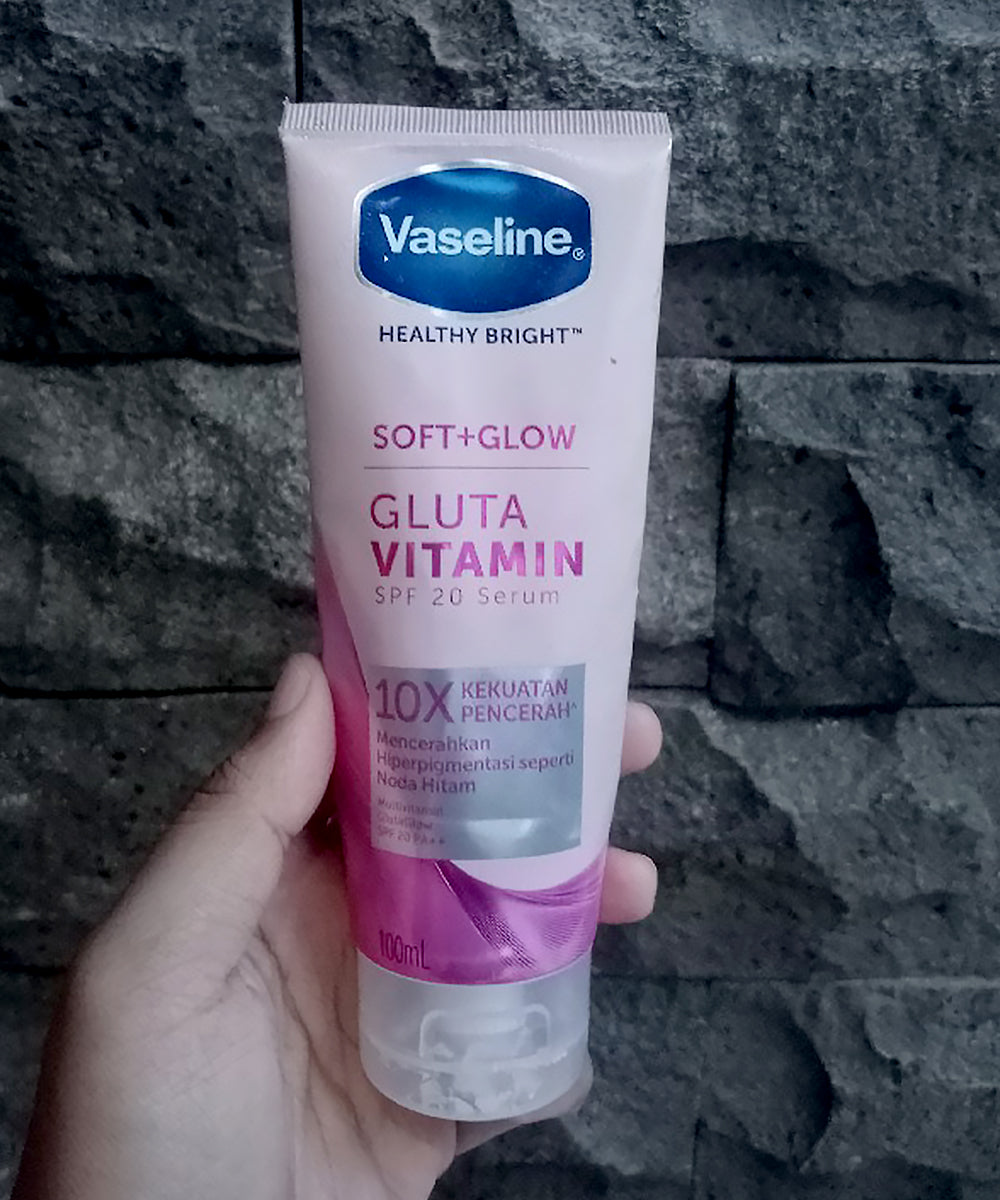 Vaseline Gluta Vitamin skincare product held against a stone wall background