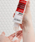 Hand holding a tube of DERCOS Shampoo & Scalp Treatment with white background
