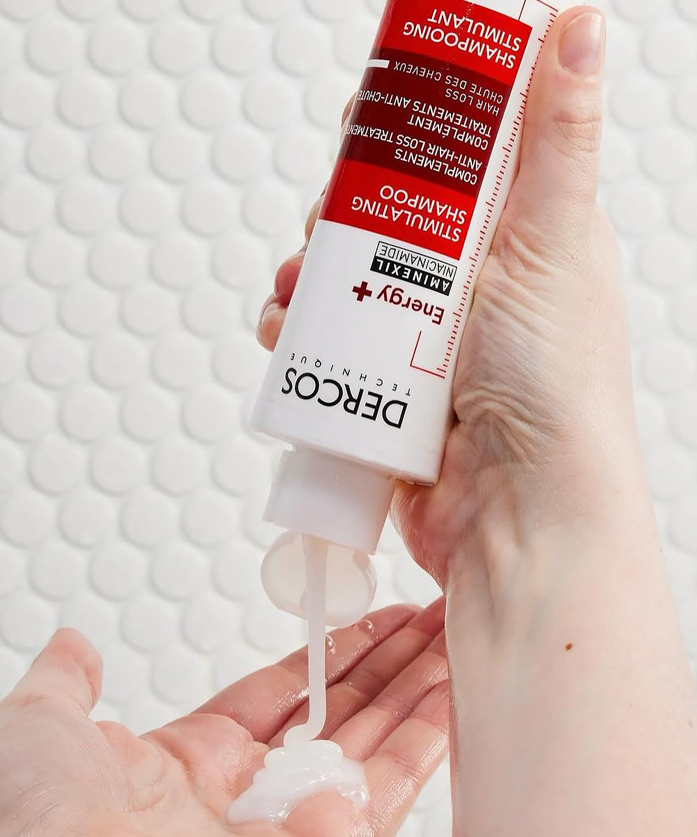 Hand holding a tube of DERCOS Shampoo & Scalp Treatment with white background