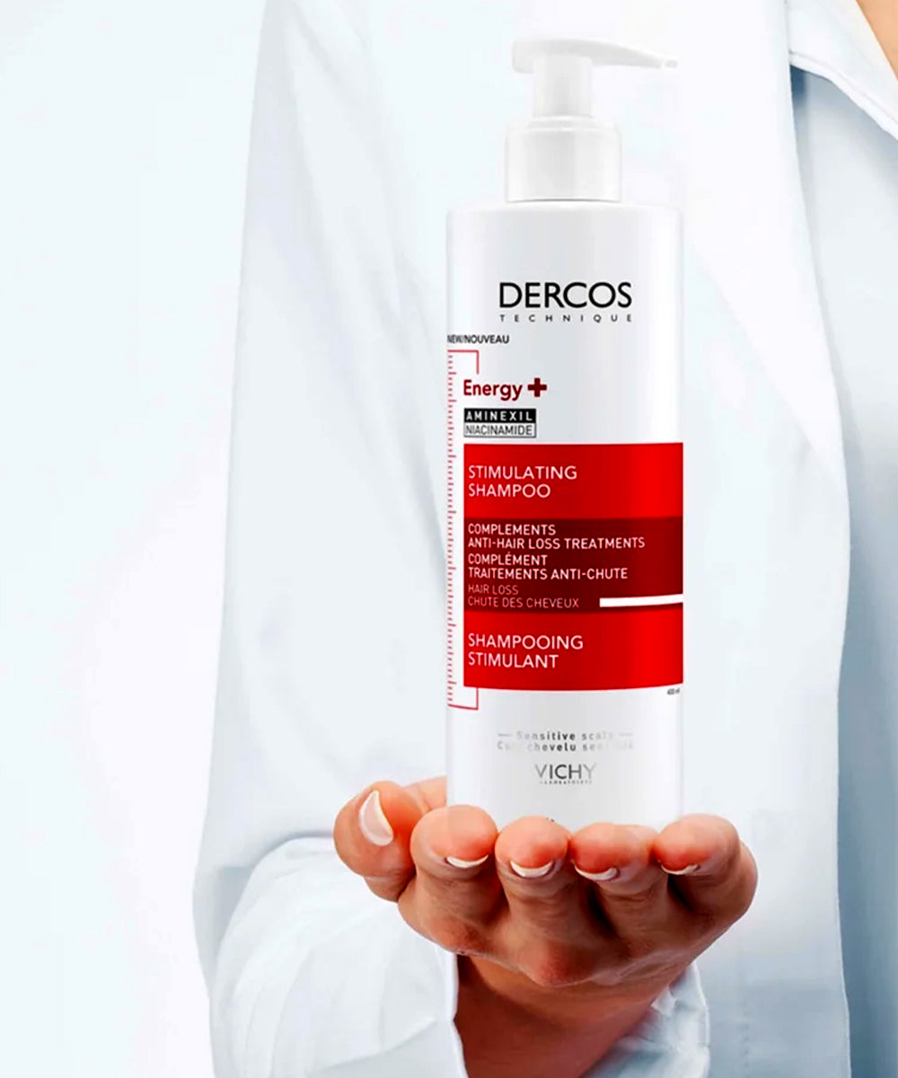 Person holding a bottle of Dercos shampoo with a white background
