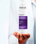 White-coated professional hand displaying Vichy Dercos Neogenic Redensifying Shampoo